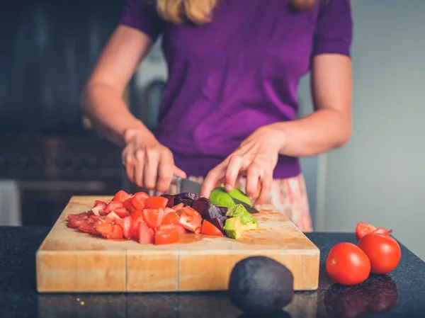 Молодая женщина готовит салат с помидорами и авокадо — стоковое фото