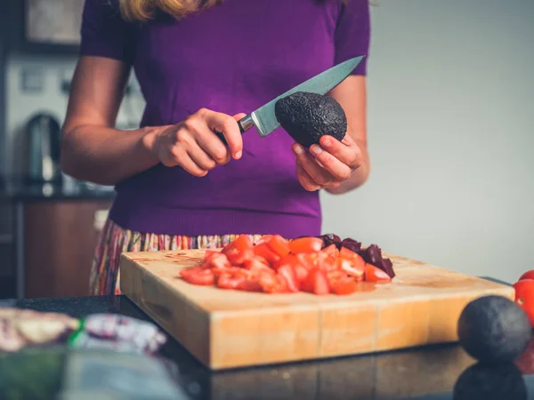 Ung kvinna förbereder sallad med tomater och avokado — Stockfoto