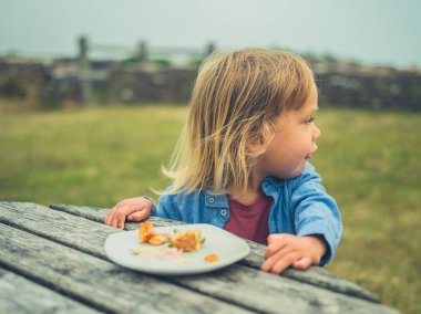 Küçük sevimli çocuk sisli bir günde piknik masasında yemek yiyor.