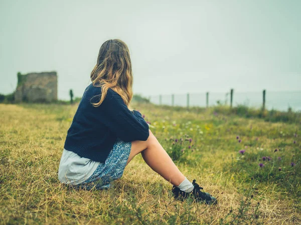 雾天年轻女子坐在海边的草地上休息的侧视图 — 图库照片