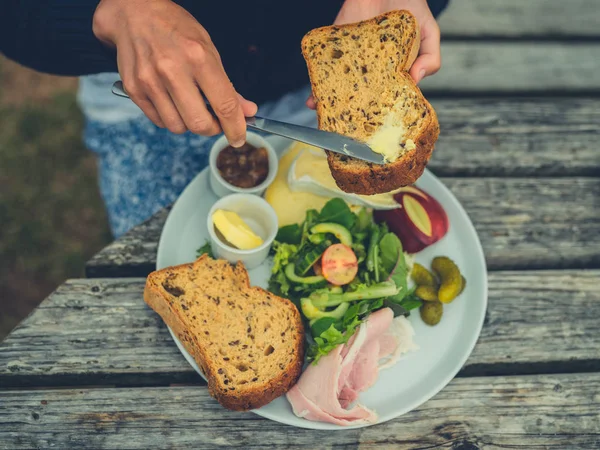 采摘的年轻女子在户外野餐桌上做三明治时涂黄油面包的照片 — 图库照片