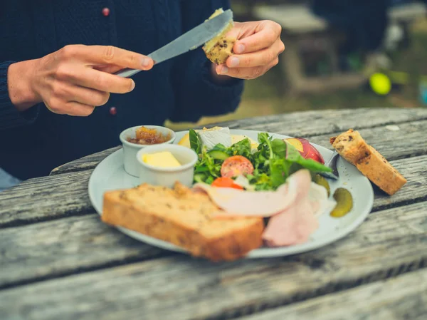 Bilde Ung Kvinne Som Smører Brød Utendørs Ved Piknikbordet Mens – stockfoto