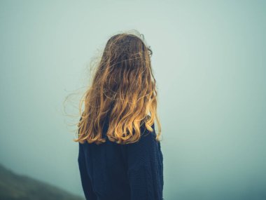 Genç bir kadın sisin içinde duruyor.