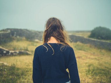 Genç bir kadın sislerin içinde kalıntılarla tarihi bir alanda duruyor.