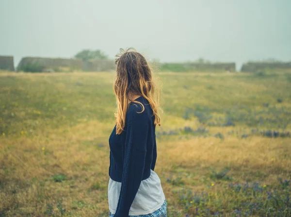 一个年轻的女人站在田里 满天飞 一片废墟 — 图库照片