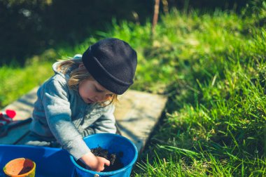 Küçük bir anaokulu çocuğu bir bahar günü bahçedeki çömleklere tohum ekiyor.