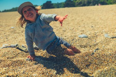 Küçük bir anaokulu çocuğu kumsalda oyun oynuyor ve kendini çakıl taşlarına gömüyor.