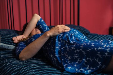 Gecelik giymiş hamile bir kadın eli karnında bir yatakta yatıyor.