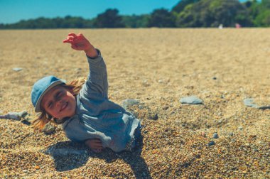 Küçük bir anaokulu çocuğu kumsalda oyun oynuyor ve kendini çakıl taşlarına gömüyor.
