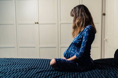 Gecelik giyen hamile bir kadın yatakta dinleniyor.