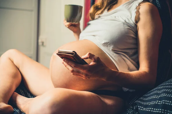 Ung Gravid Kvinna Dricker Mugg Och Använder Sin Smartphone Sängen — Stockfoto