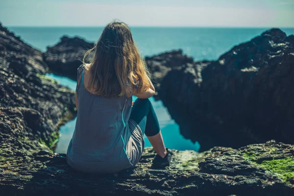 一个年轻的女人正在海边的一个岩石池边休息 — 图库照片