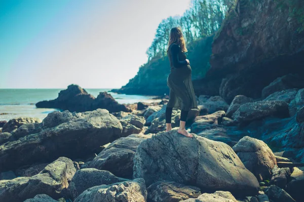 一个年轻的孕妇在海边的一些大石头上散步 — 图库照片