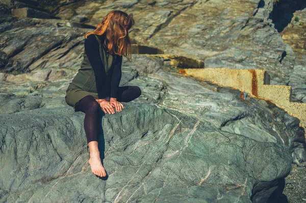一个年轻的女人坐在海边的岩石上 — 图库照片