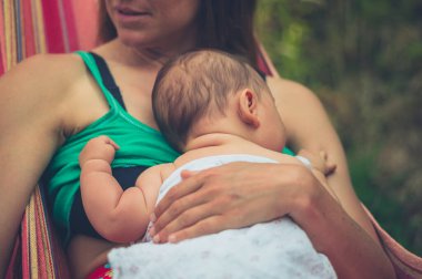 Genç bir anne yazın bebeğiyle birlikte bir hamakta dinleniyor.