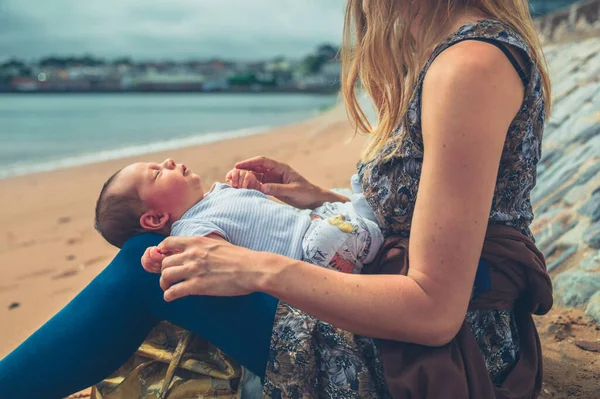 一位年轻的母亲和她刚出生的孩子坐在海滩上 — 图库照片