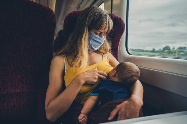 顔のマスクをした若い母親が電車の中で赤ん坊を母乳で育てている — ストック写真