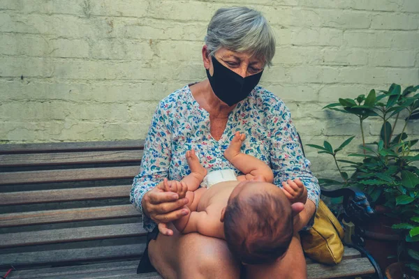本物のショットの祖母とともに顔マスク保持彼女の赤ちゃん孫 — ストック写真