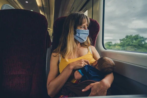 顔のマスクをした若い母親が電車の中で赤ん坊を母乳で育てている — ストック写真