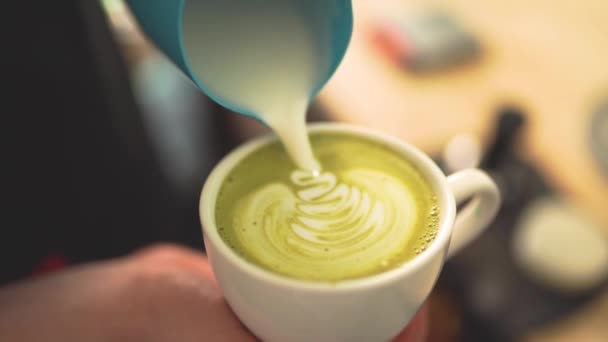 Slow motion of barista pouring milk over creating Matcha latte art — ストック動画