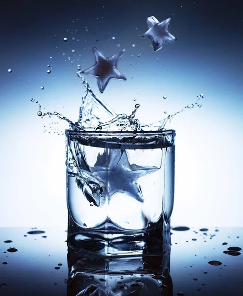 ice cubes in the form of stars on a blue background fall into a glass of water