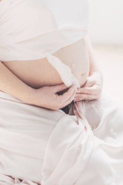 Elinde beyaz tüy tutan hamile bir kızın karnı.