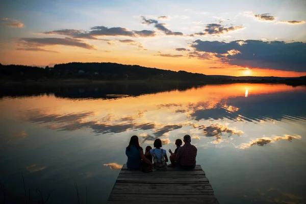 Familjen sitter på stranden av en stor sjö vid solnedgången Stockbild