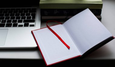 Dizüstü bilgisayar ve kitapların yanında duran metinler için beyaz sayfalı katlanmış defter