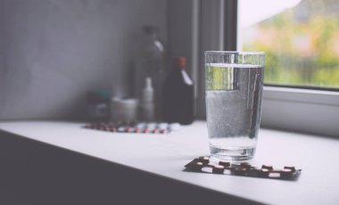 Şeffaf cam, su ve beyaz bir masanın üzerinde haplar. 