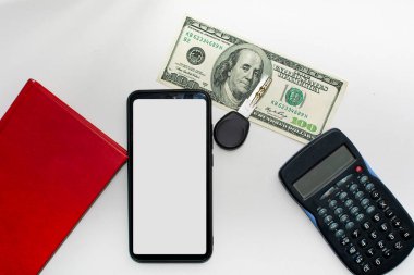 Hesap makinesi, beyaz ekranlı anahtar telefon. 100 dolar ve beyaz arkaplanda defter.