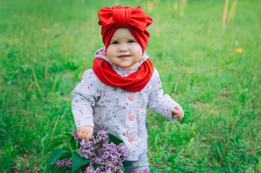 Kırmızı şapkalı küçük kız bahçede mor leylağın yanında.