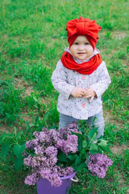 Kırmızı şapkalı küçük kız bahçede mor leylağın yanında.