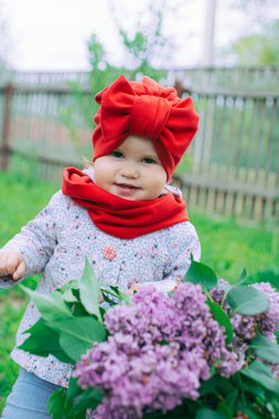 Kırmızı şapkalı küçük kız bahçede mor leylağın yanında.
