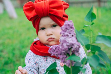Kırmızı şapkalı küçük kız bahçede mor leylağın yanında.