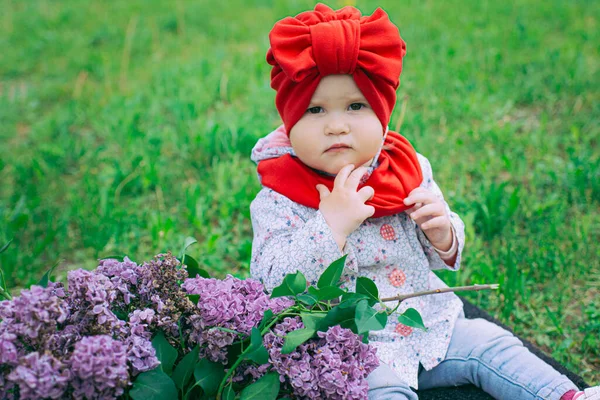 Kırmızı şapkalı küçük kız bahçede mor leylağın yanında.