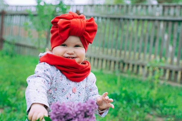 Kırmızı şapkalı küçük kız bahçede mor leylağın yanında.