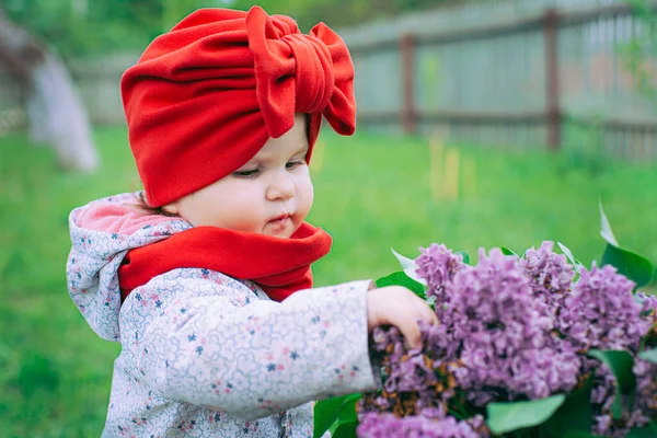 Kırmızı şapkalı küçük kız bahçede mor leylağın yanında.
