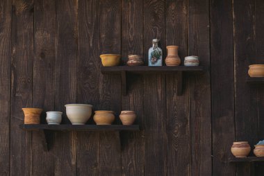 Tahta bir rafta kil sürahiler ve ahşap siyah bir duvar.