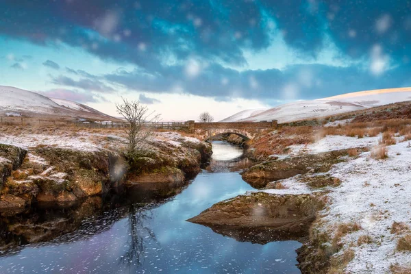 Pont Ar Elan, vale Elan, vales. Cena nevada de Afon Elan fluindo sob uma ponte com árvore solitária e sol primitivo — Fotografia de Stock