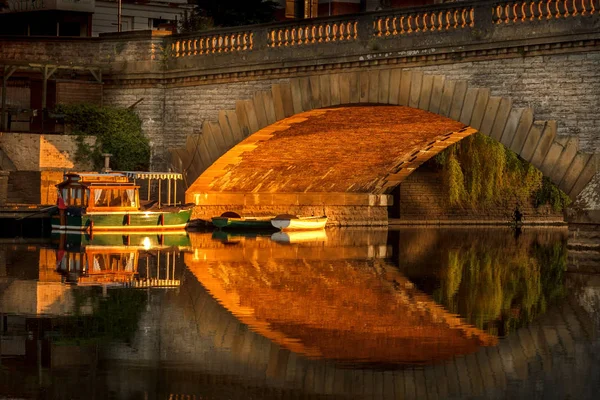 Sun lighting workman bridge in Evesham with boats moored underneath