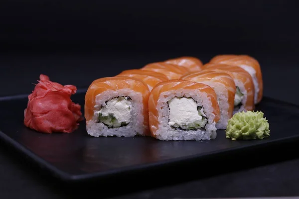 sushi roll philadelphia with salmon. top view philadelphia roll sushi with smoked salmon, cucumber, and cream cheese decorated with red sauce served on black background