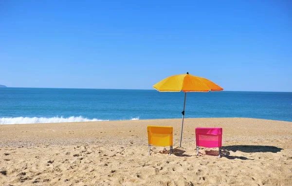 Two colorful beach chairs and umbrella with blue sea water — Stock Photo, Image