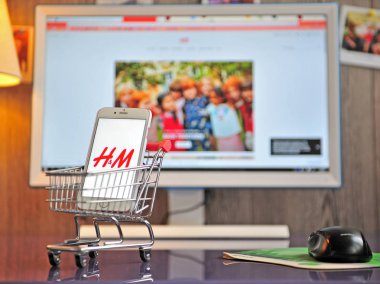Arka planda web sitesi olan H&M logolu akıllı telefon