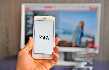 Arka planda H&M logosunu ve web sitesini gösteren akıllı telefon ile el