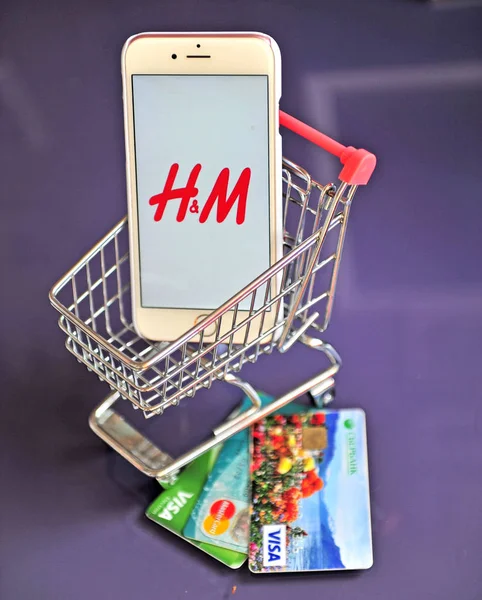 Telefone celular com logotipo H & M no carrinho de compras e cartões de crédito em — Fotografia de Stock