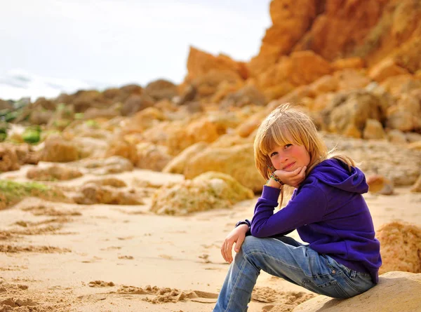 Smiling blond hair boy sitting at the rocky beach — Stock Photo, Image