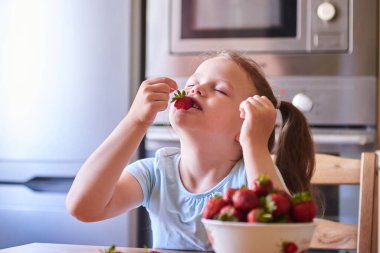Güzel Avrupalı çocuk mutfakta çilek yiyor ve süt içiyor..