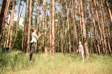 Bir anne ve iki küçük çocuk güzel bir çam ormanında topla oynuyorlar.. 