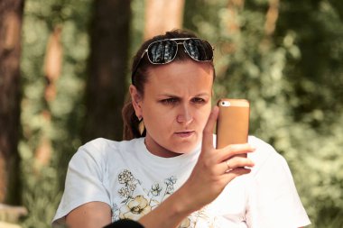 Genç bir kadın doğada telefonla haberleri izliyor. Ailenle ormanda yürüyüş yapmak. Sağlıklı yaşam tarzı kavramı