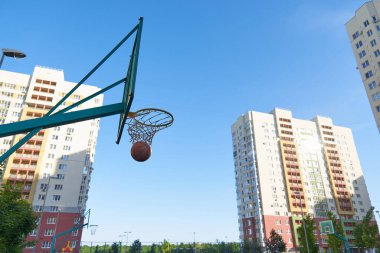 Bir basketbol sepeti ve modern konut binalarının arka planında sokak basketbolu için bir kalkan. Topla temiz hava egzersizi yap. Basketbol antrenmanı.